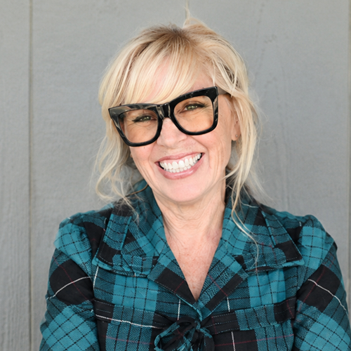 Person with blonde hair wearing sunglasses and a teal checkered shirt in front of a gray background.