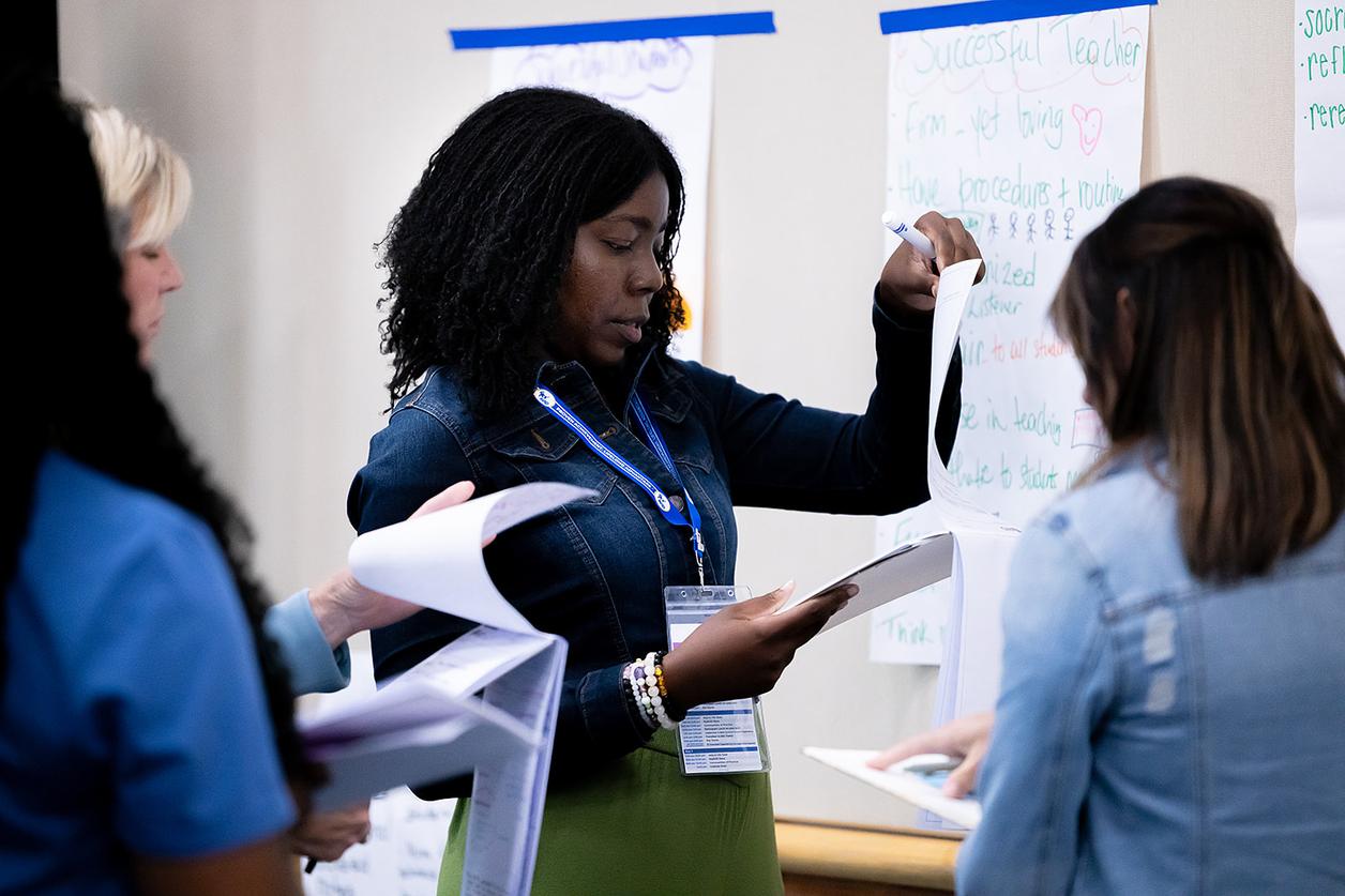 Group of individuals engaged in a collaborative discussion or brainstorming session, facing a wall with instructional posters. Group of individuals engaged in a collaborative discussion or brainstorming session, facing a wall with instructional posters.