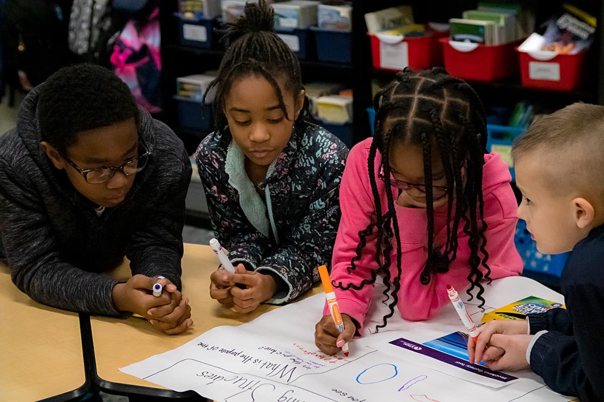 Children working together at a table on a colorful poster with markers in a classroom setting. Children working together at a table on a colorful poster with markers in a classroom setting.