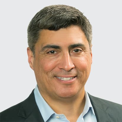 A person wearing a dark blazer and light blue collared shirt with short, styled hair. A person wearing a dark blazer and light blue collared shirt with short, styled hair.