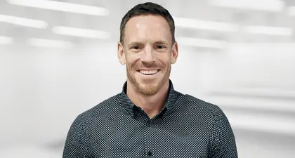 Person smiling and wearing a patterned shirt against a black background. Person smiling and wearing a patterned shirt against a black background.