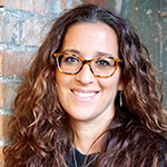 Person with curly hair standing in front of a brick wall.