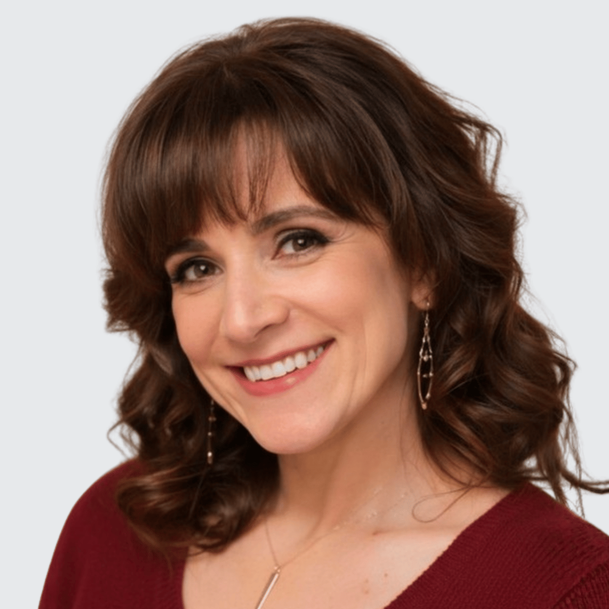 Individual with shoulder-length wavy hair wearing a red sweater on a gray background. Individual with shoulder-length wavy hair wearing a red sweater on a gray background.