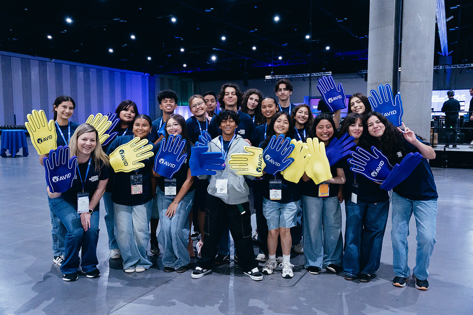 Group photo of people in a large room holding blue and yellow foam hands with 'AVID' written on them.