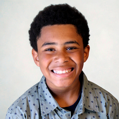Person with curly hair wearing a patterned gray shirt against a neutral background.