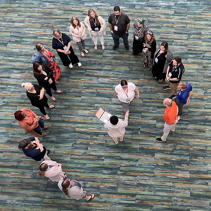 A group of people standing in a circle in an indoor setting with a blue-green floor.