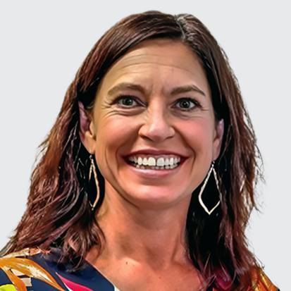 A person wearing a colorful, patterned blouse with leafy designs that include yellow, orange, and geometric shapes. The background is a plain light color.