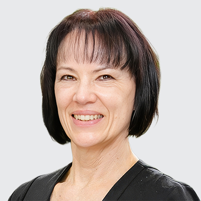 A portrait photo with a blurred face, featuring a person with shoulder-length, dark hair and wearing a black top. The background consists of green plants giving a natural ambiance.