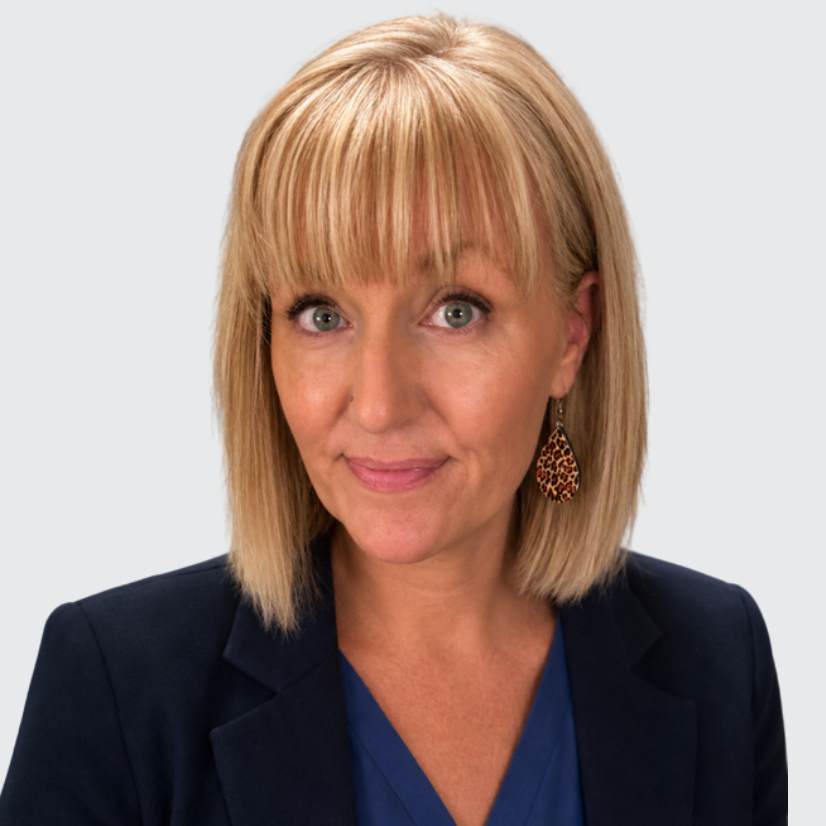 Person with shoulder-length blonde hair, wearing a blue blazer and leopard print earrings, against a neutral background.