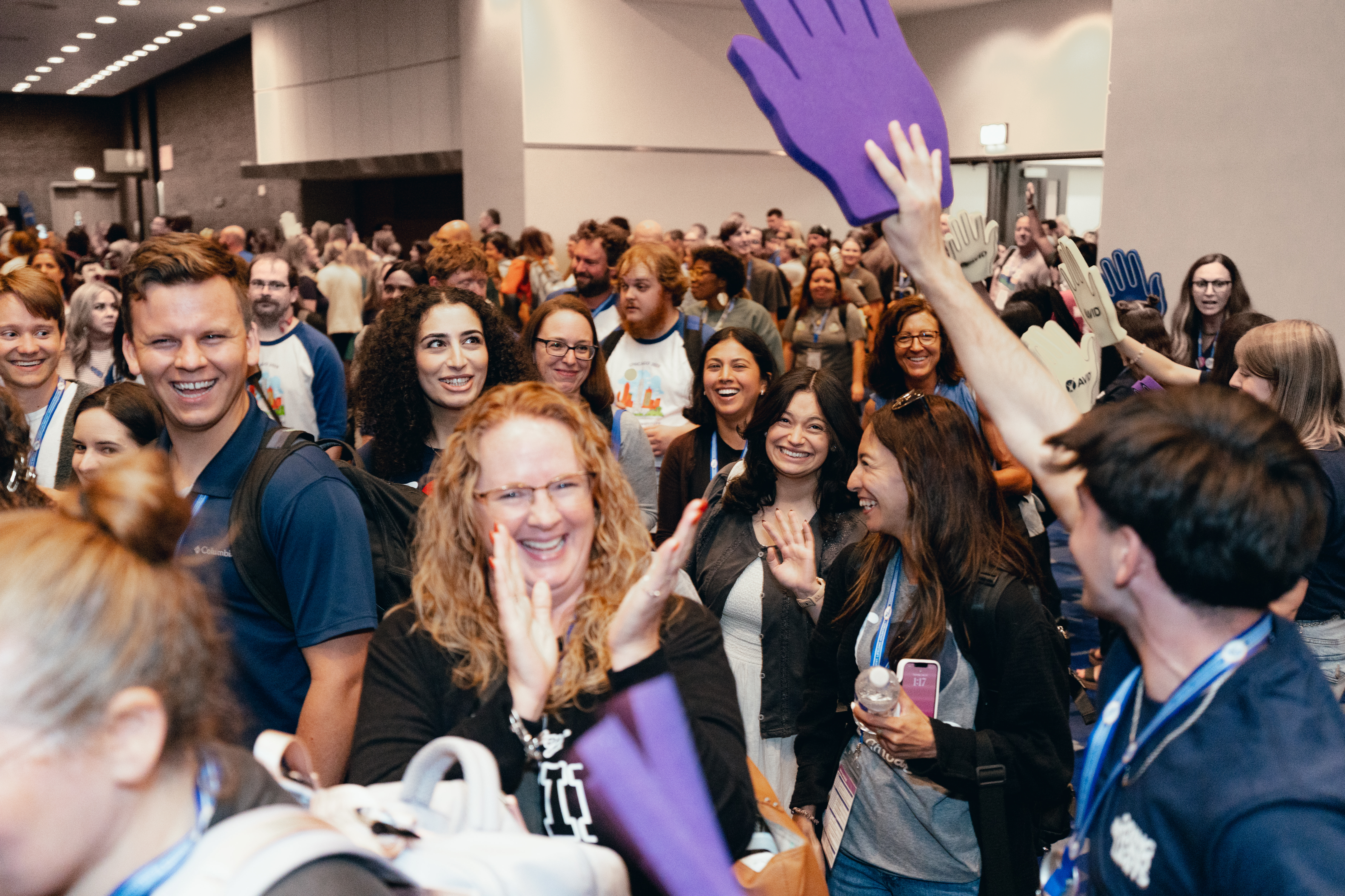 A large group of people in a conference hall with some participants holding up foam hands.
