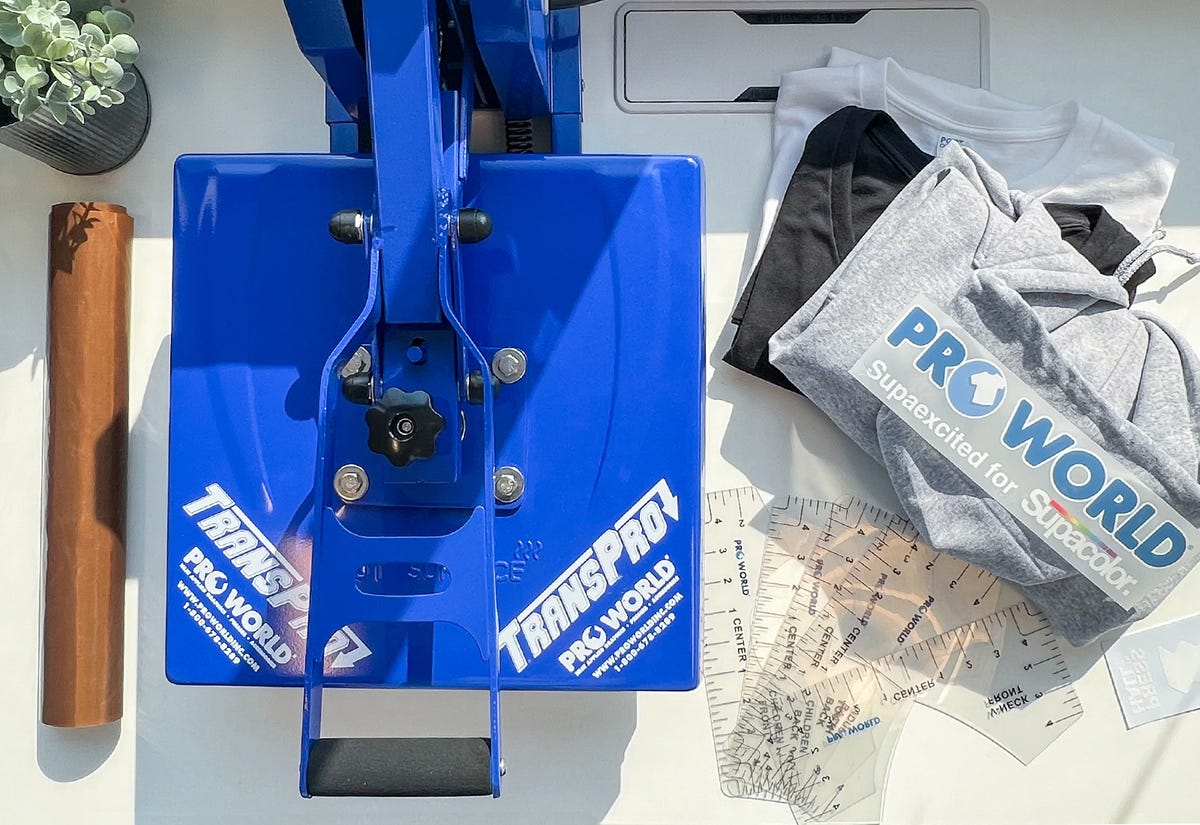 Flat lay of the starter pack bundle with a clamshell heat press, blanks, and Supacolor.