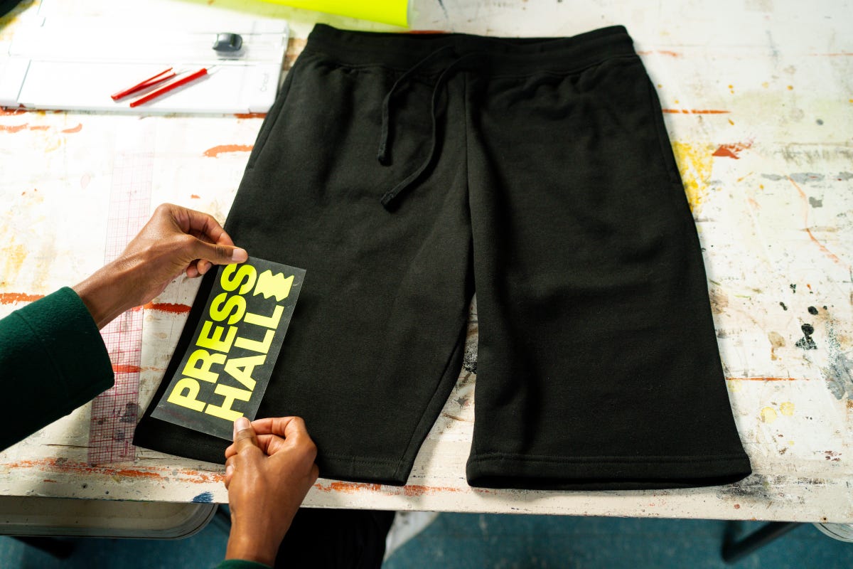 Fluorescent yellow heat transfer vinyl with the Press Hall design placed on the bottom left of a black sweat shorts.