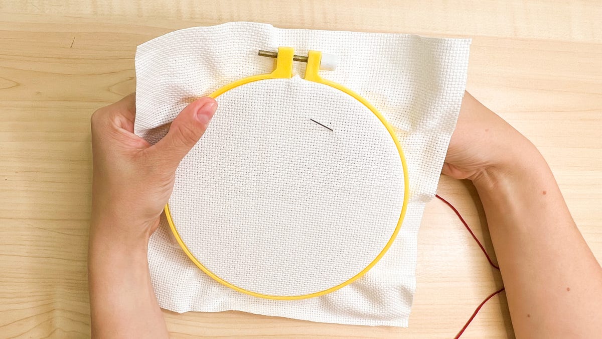 Pushing the needle from the back of the hoop and through the front.