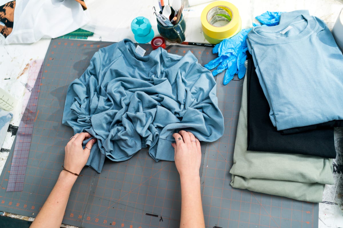 Pair of hands scrunching a blue long sleeve shirt to create a design for bleaching.