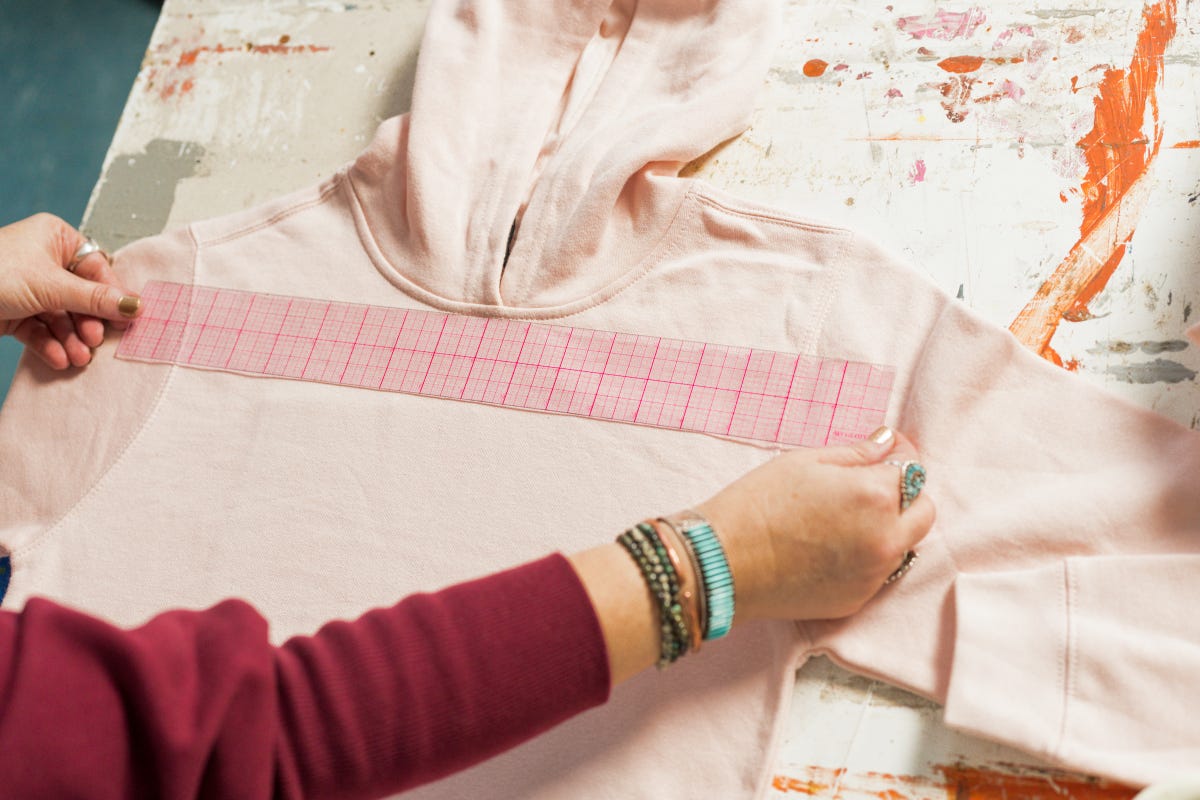 Planning the placement of the screen printed design using an acrylic ruler on the pink sweatshirt hoodie.