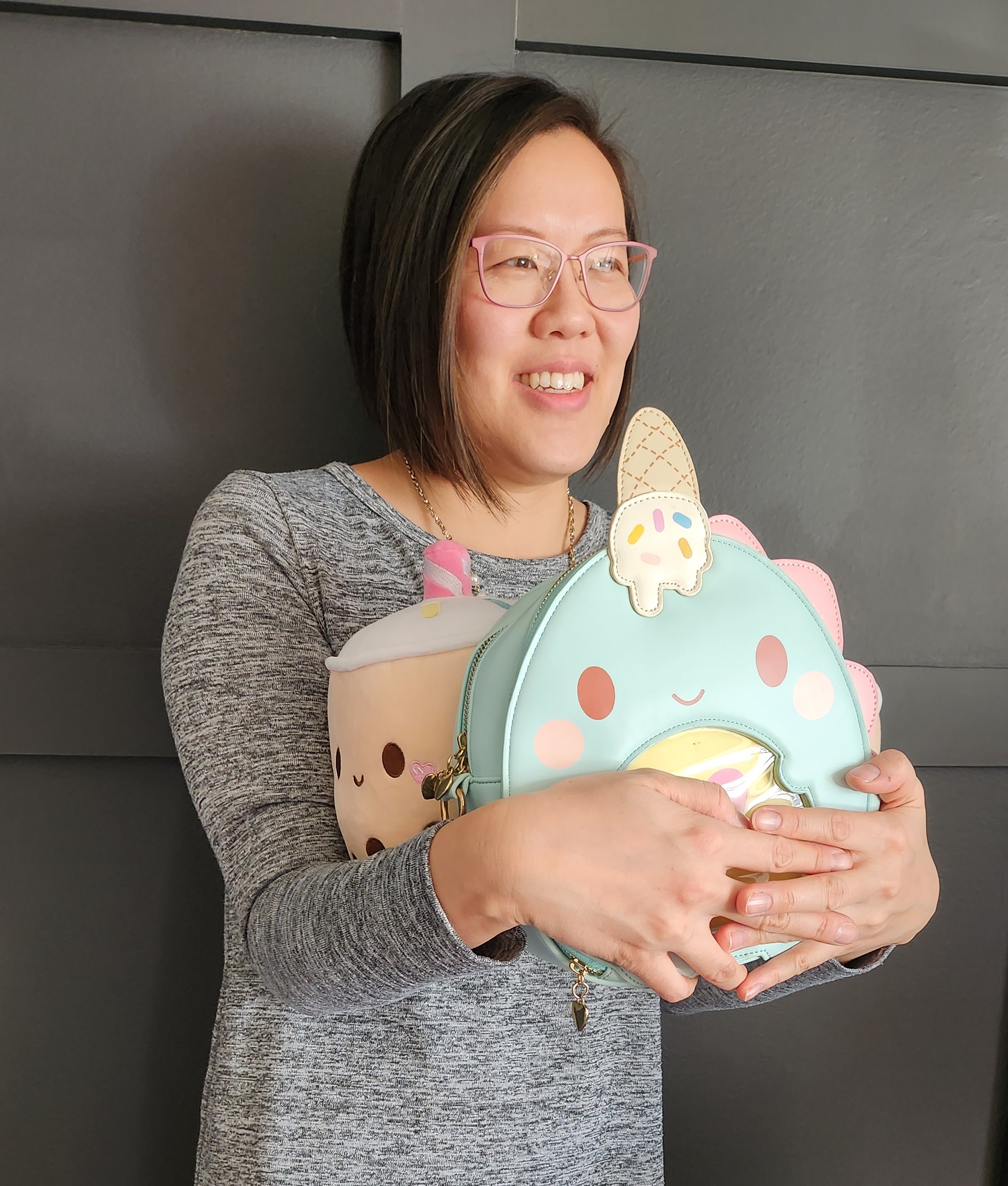 Lina smiling off camera holding a boba plushie and dinosaur with an ice cream backpack.