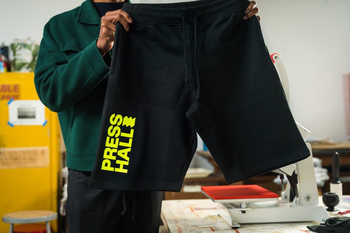 Holding up a black sweat shorts with the Press Hall logo design heat pressed on.