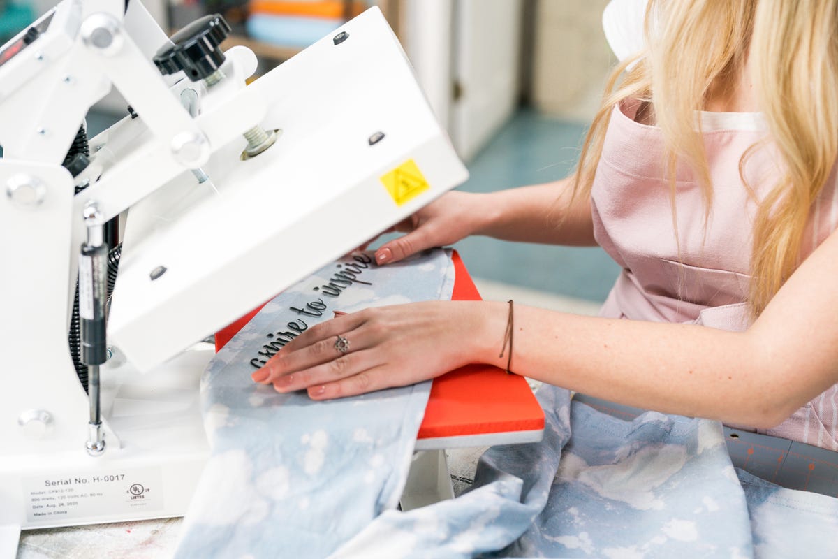 Megan placing the heat transfer vinyl cut with "Aspire to inspire" along the sleeve of the reverse dyed shirt.