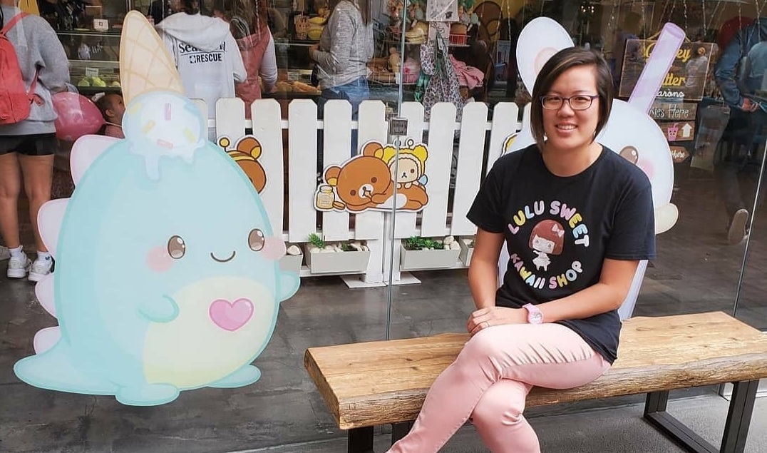 Lina sitting on a bench next to a life-size kawaii dinosaur with ice cream on its head, smiling at the camera.