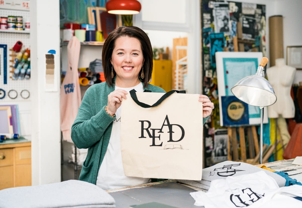 Jennifer holding up tote bag with "READER" screen printed on the front.