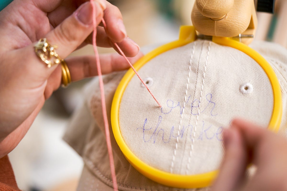 Sophie creating the first stitch by pushing the threaded needle through from the underside of the cap and pulling the floss through at the front.