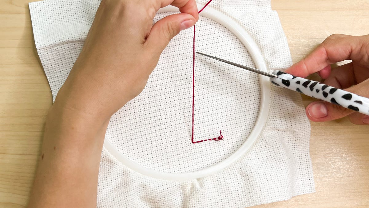 Cutting the embroidery floss leaving at least 3 inches of excess embroidery floss.