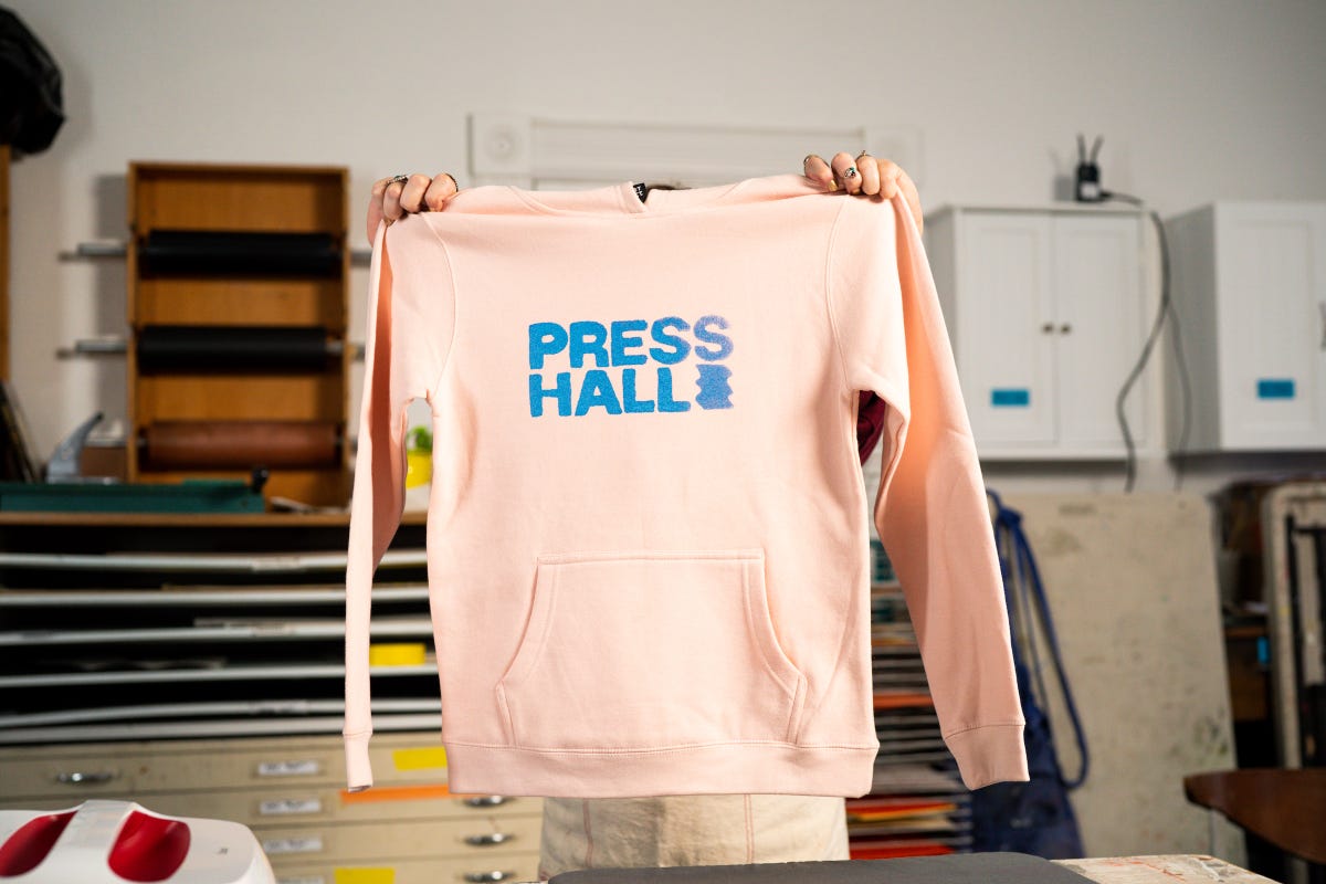 Holding the final product of the pink sweatshirt hoodie screen printed with the Press Hall logo.