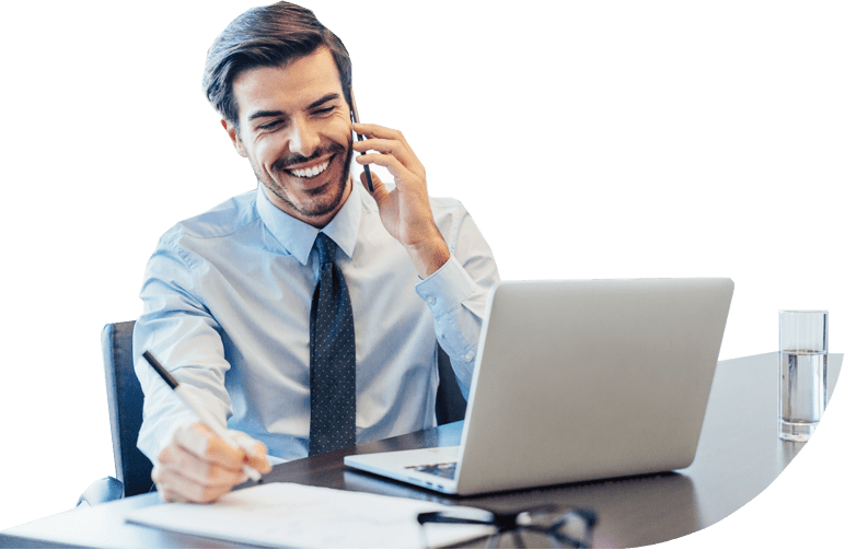 Person smiling while talking on the phone as they sit at a desk with their laptop.