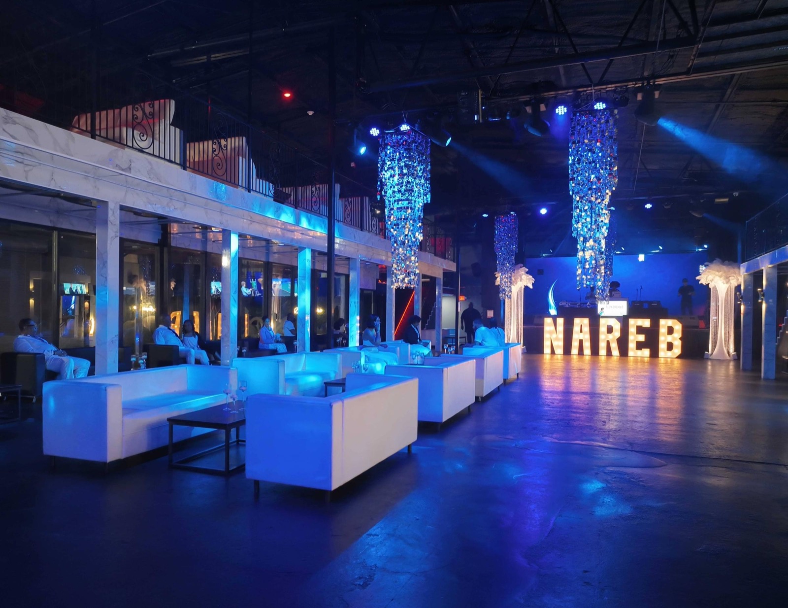 Event venue with white lounge seating, chandeliers and an illuminated NAREB sign.