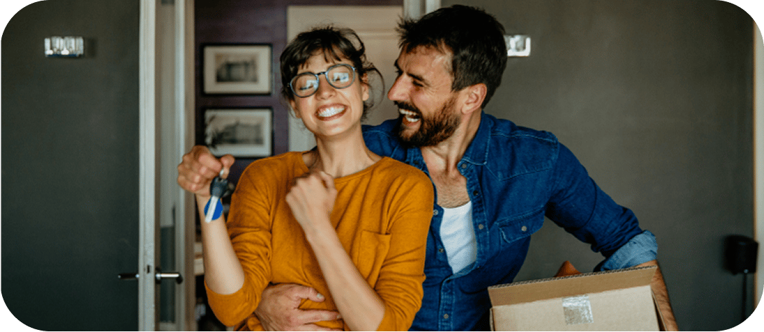 Couple with keys and a box laughing.