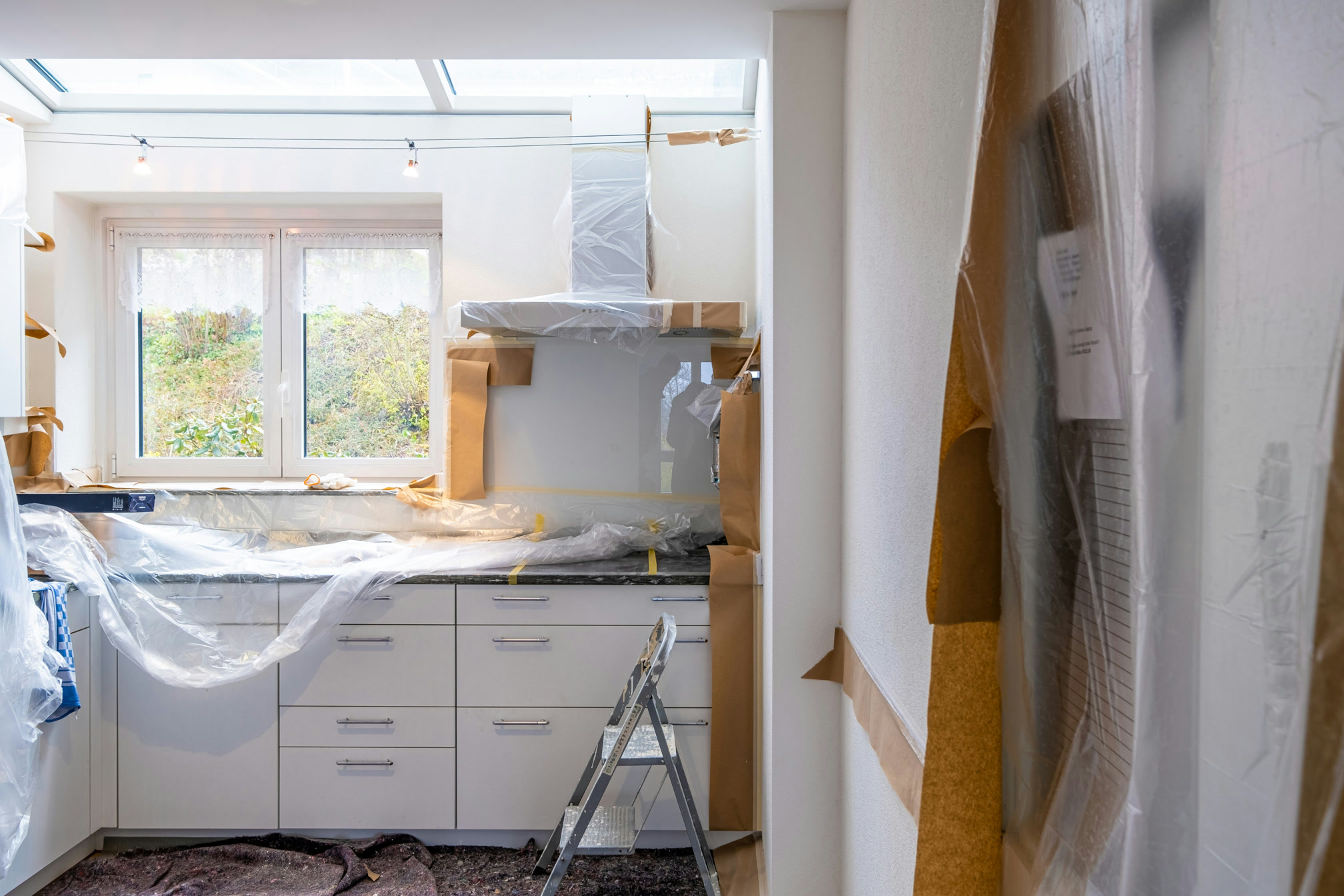 Kitchen under renovation with cabinets and counters wrapped in plastic.