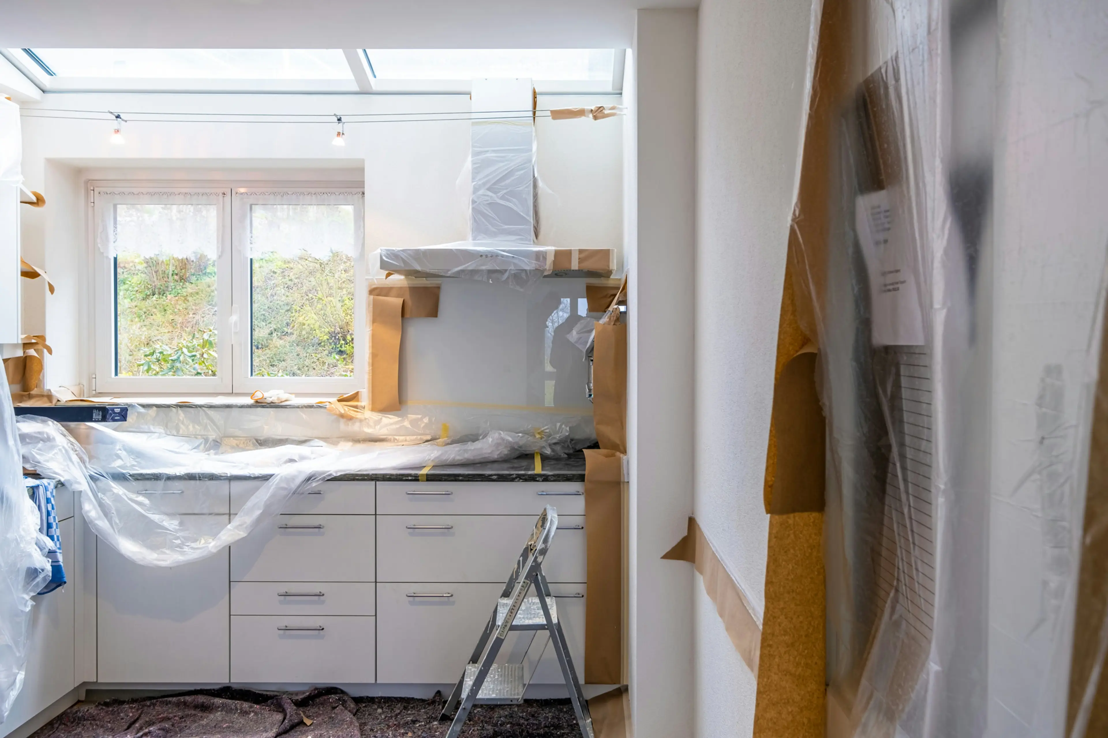 Kitchen under renovation with cabinets and counters wrapped in plastic.