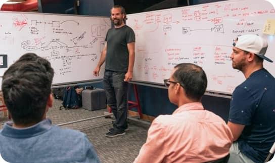A man presents information on a drawing board to a group of people.