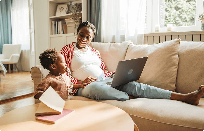 Pregnant mom on laptop next to child