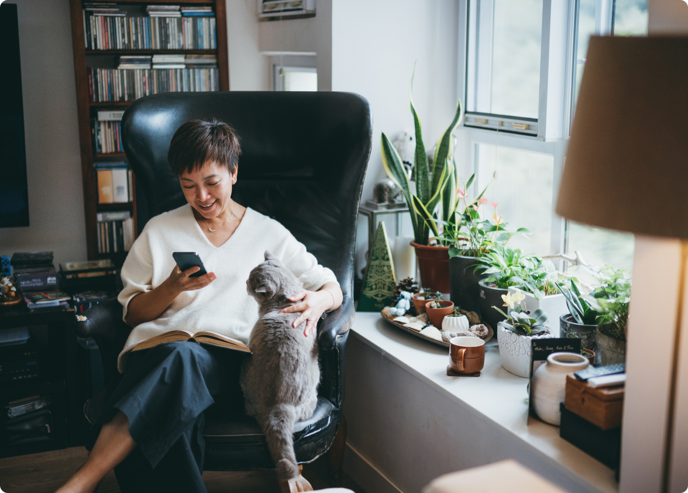 Woman sitting in a chair looking down at her smart phone and petting her gray cat