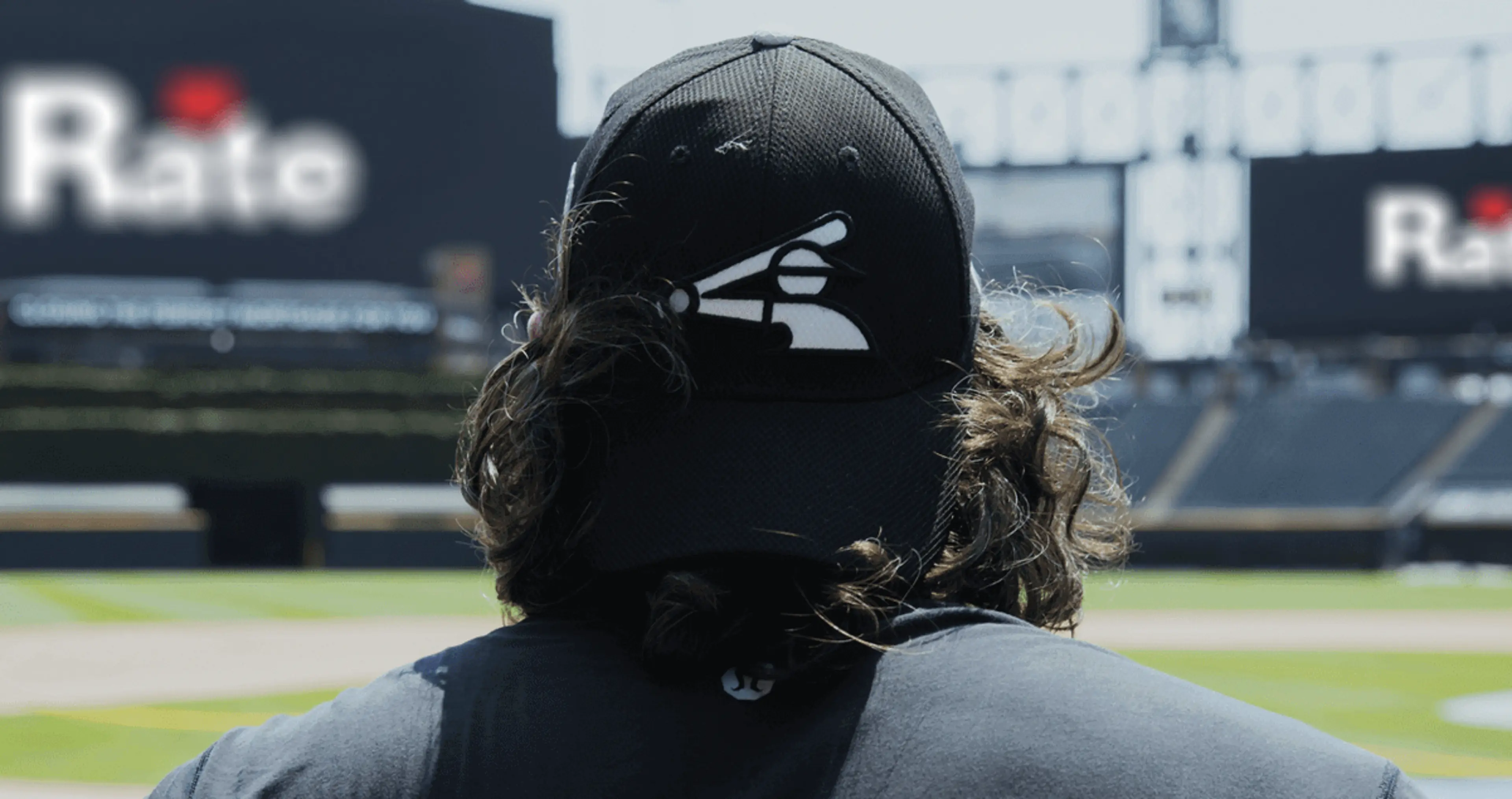 The back of the head and shoulders of a baseball player standing in a baseball field.