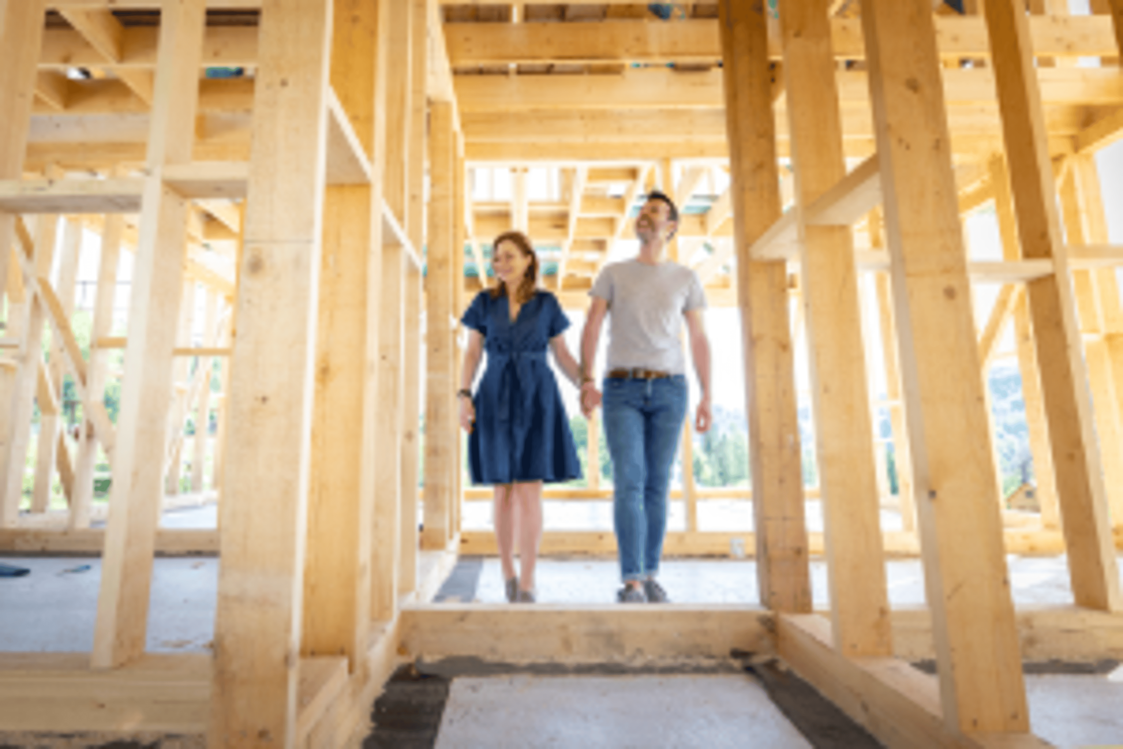 A couple holding hands while walking through the wooden frame of their home under construction.