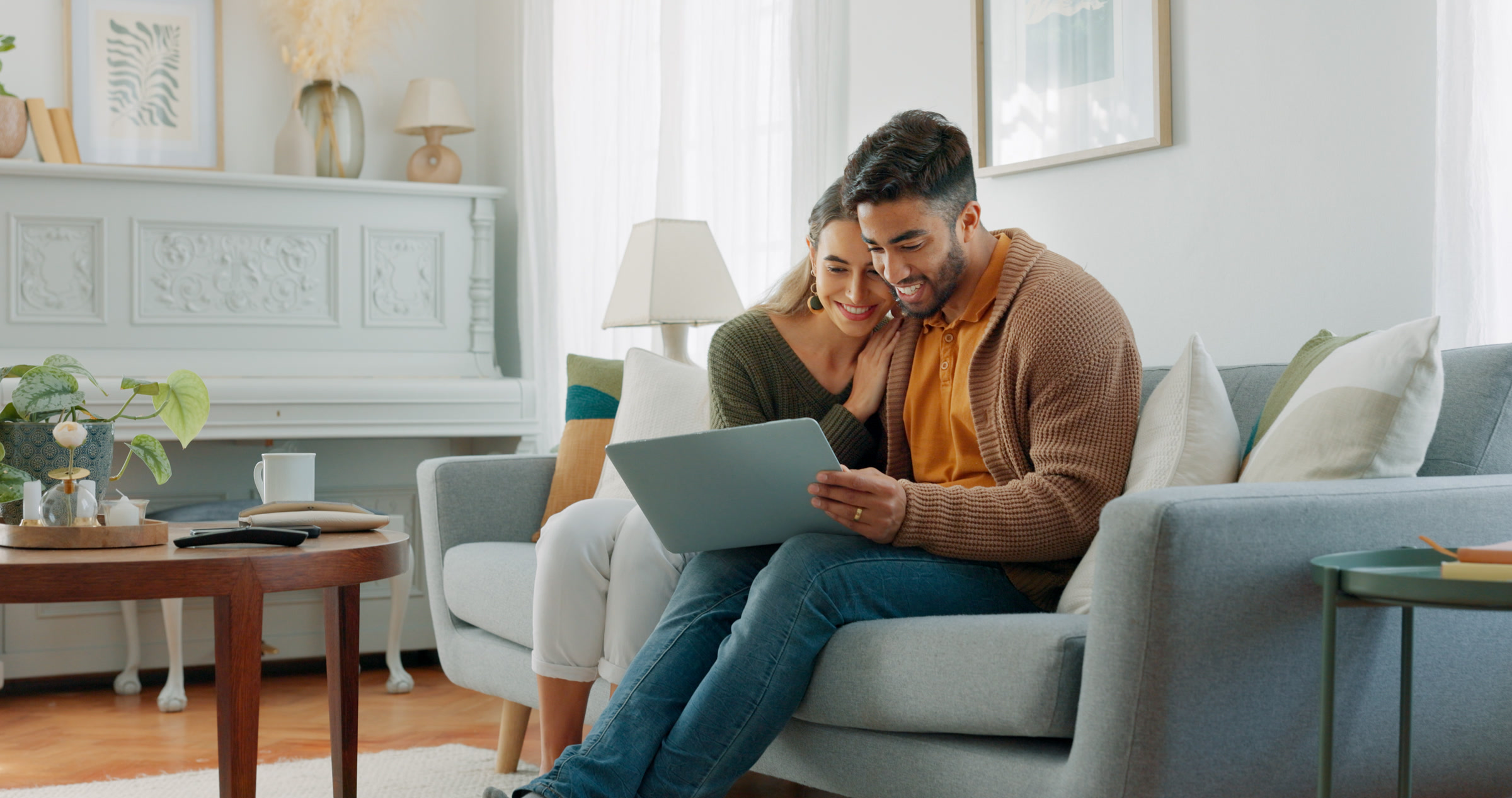 Couple smiling at a laptop together on a sofa at home.