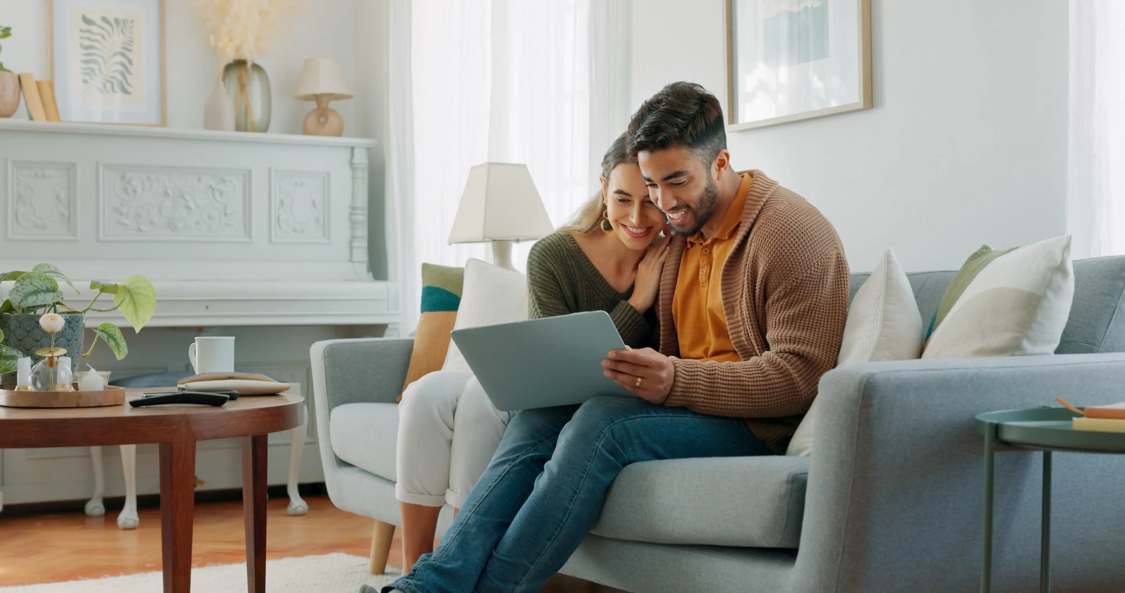Couple smiling at a laptop together on a sofa at home.