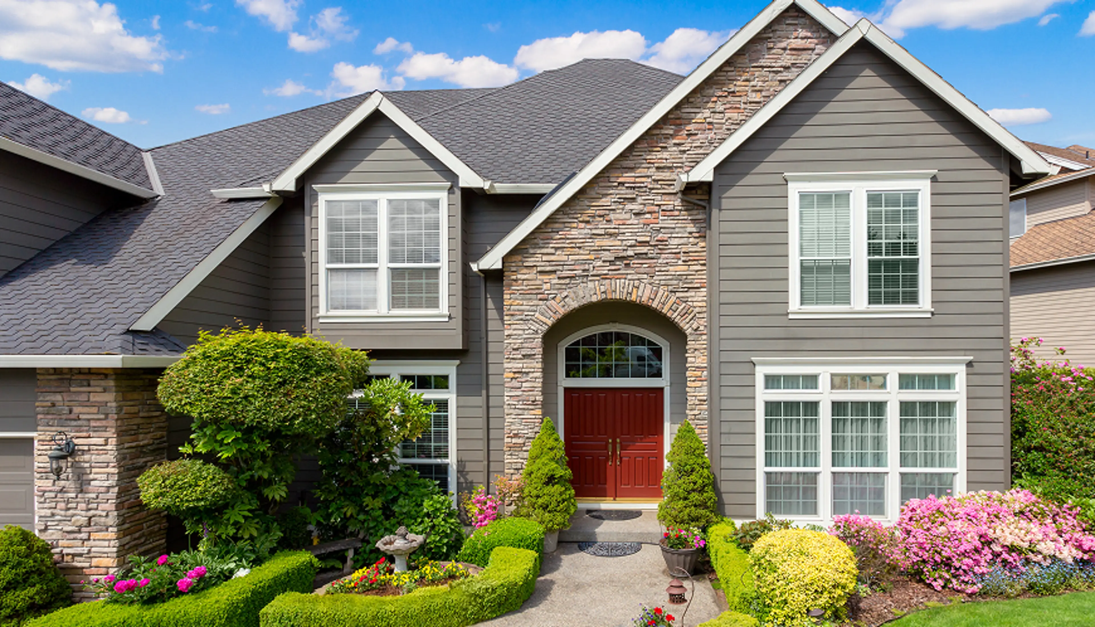 A two-story house with a walkway that has plants along the sides.