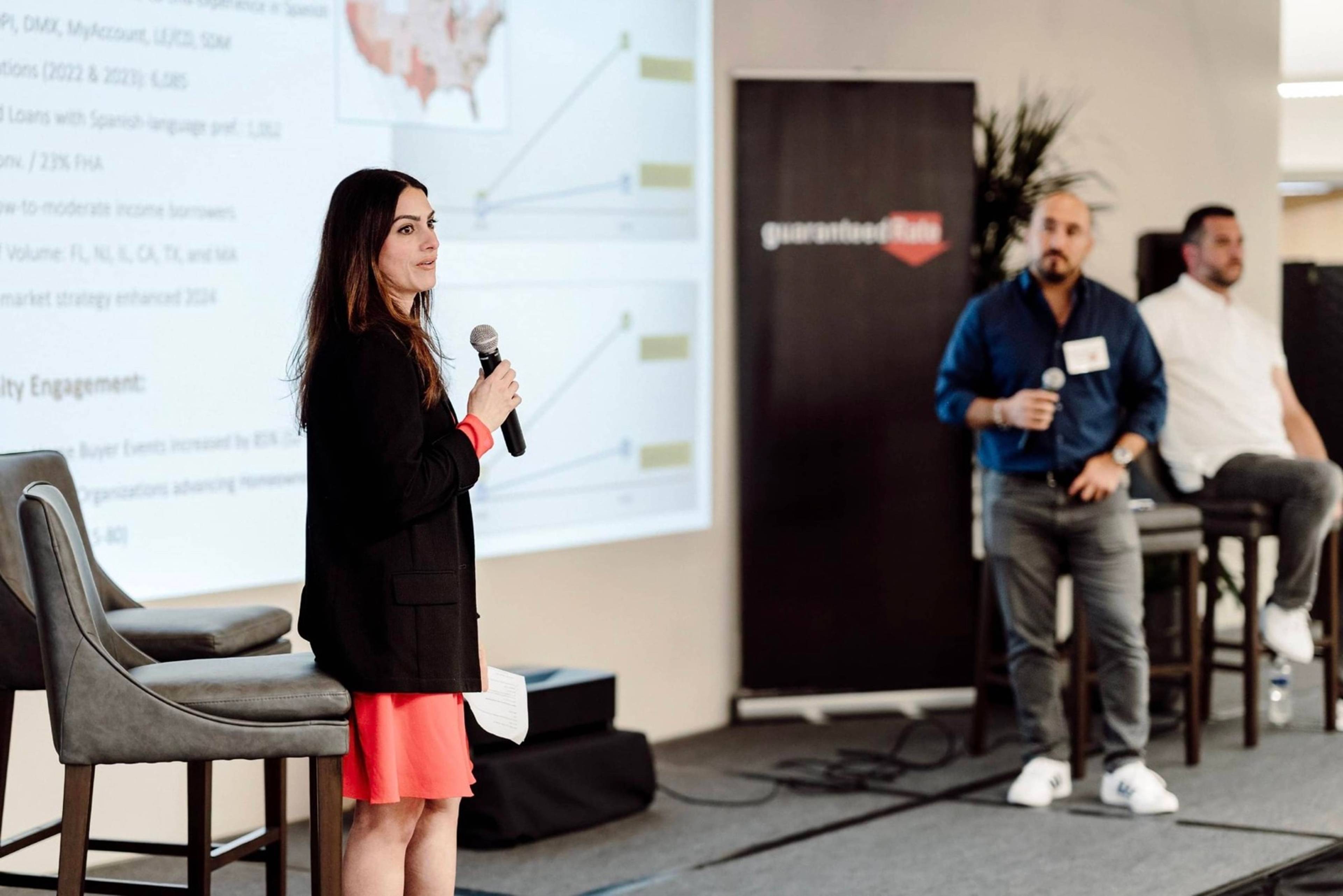 Arlyn Kalinski presenting LEAD results on stage while two panelists wait beside a Guaranteed Rate banner.