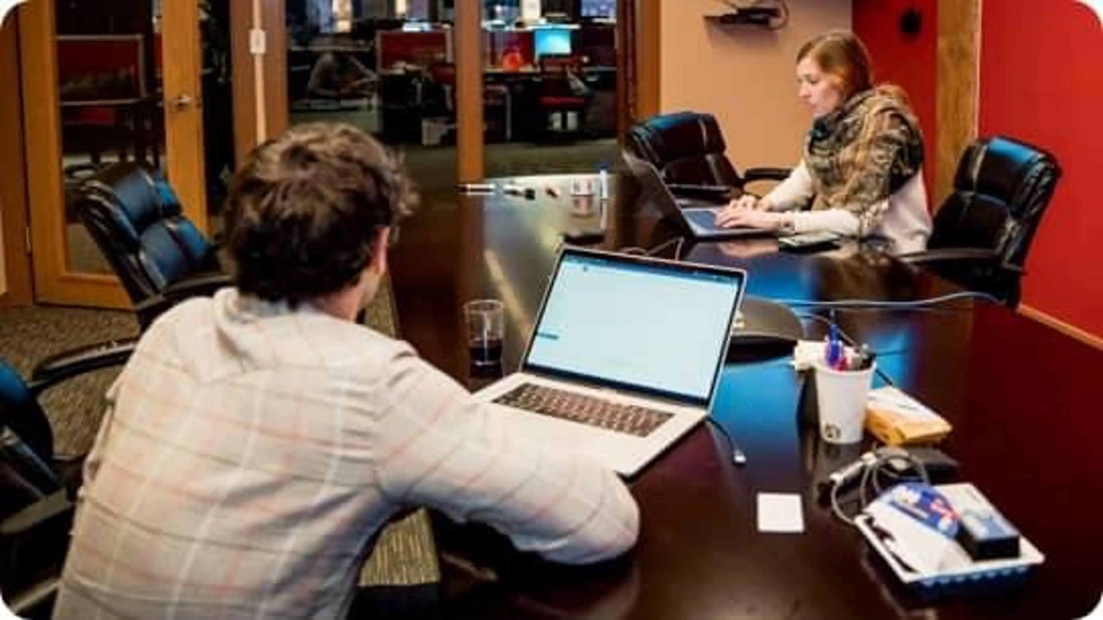 Two employees use their laptops at a shared desk.