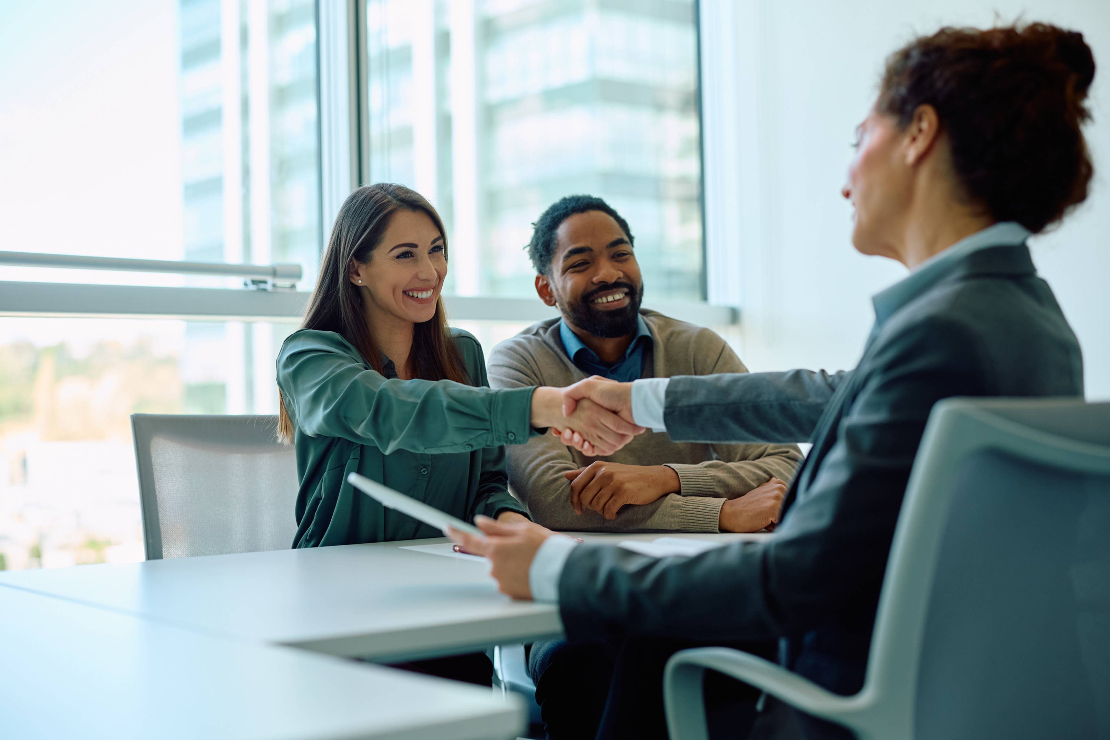 A couple sitting at a desk shaking hands with a financial lender.