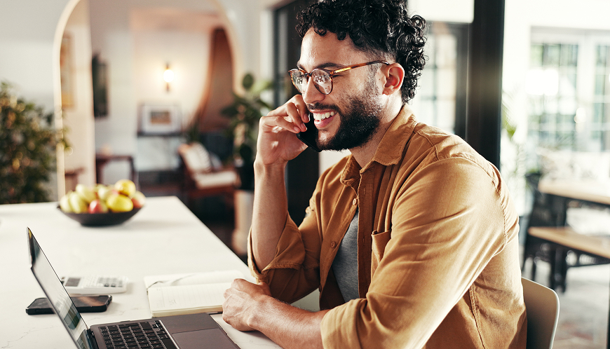 A person sits at a desk smiling while on a phone call.