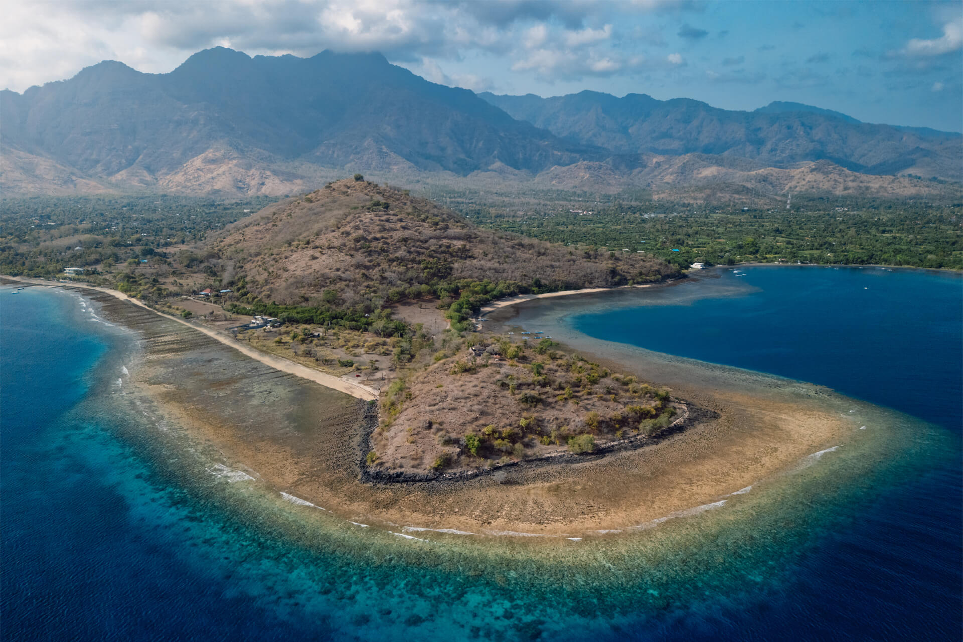 Pemuteran beach surrounded by turquoise waters and coral reefs, with dry hills and mountains in the background.