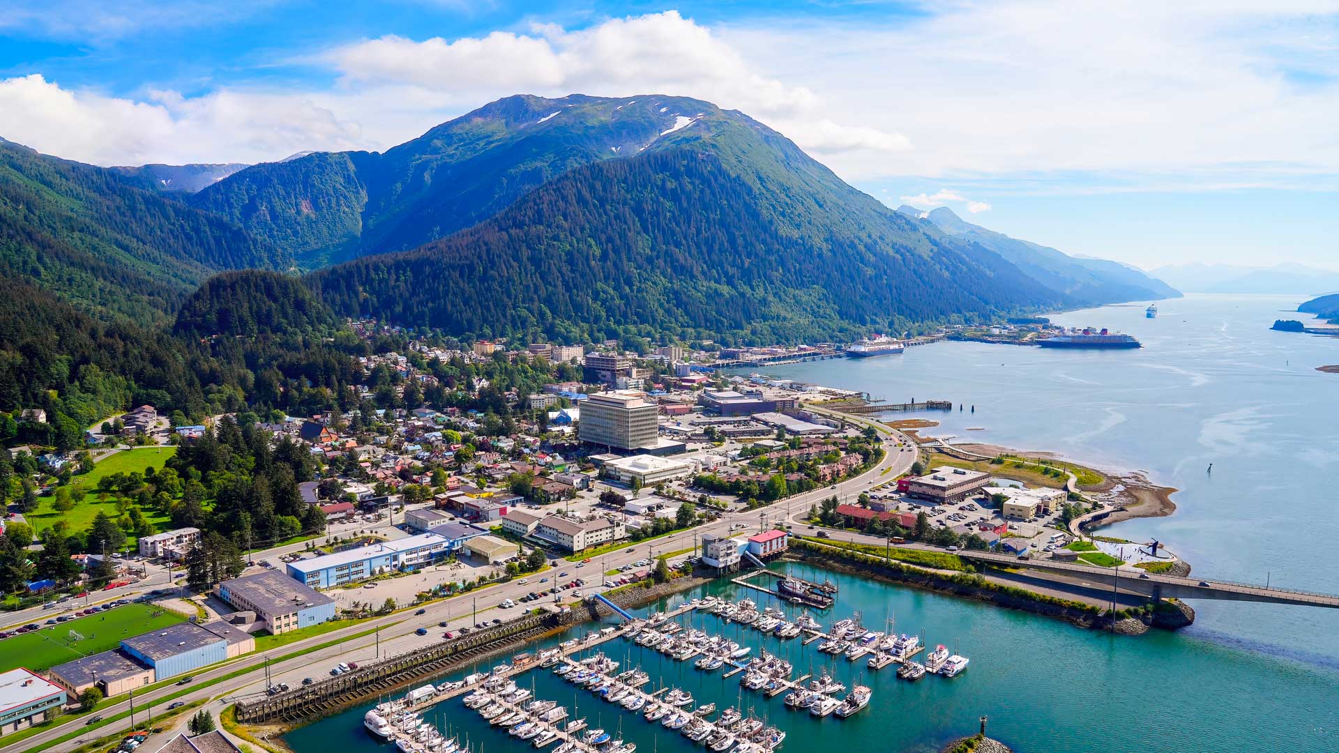 Vue aérienne de Juneau, ville côtière d’Alaska entourée de montagnes verdoyantes, avec sa marina, et son centre urbain.