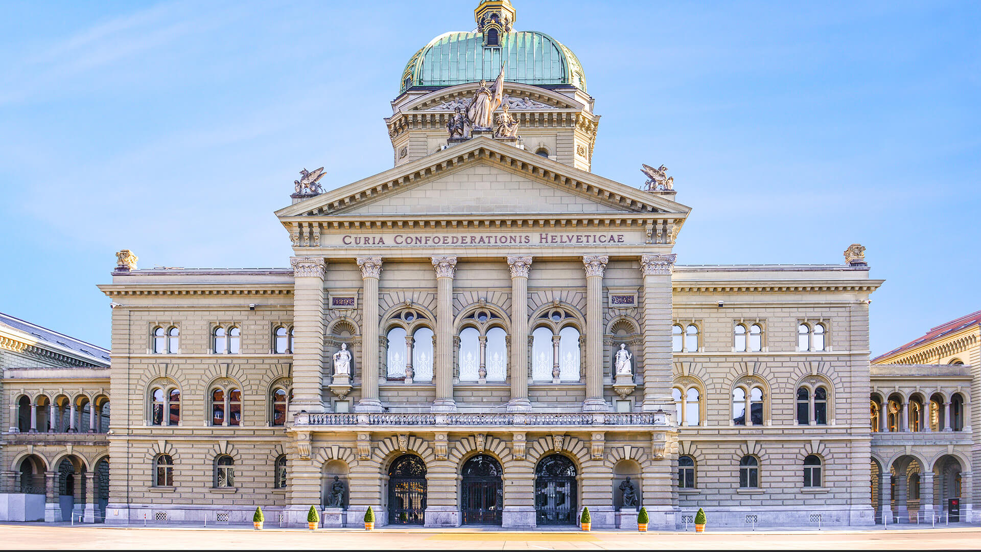 Bâtiment du Parlement suisse à Berne, avec sa façade imposante et sa coupole, sous un ciel bleu clair.