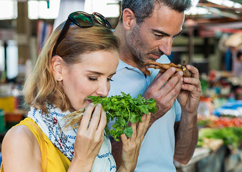 Dans un marché, un couple adepte du slow travel hume des herbes et racines fraîches.