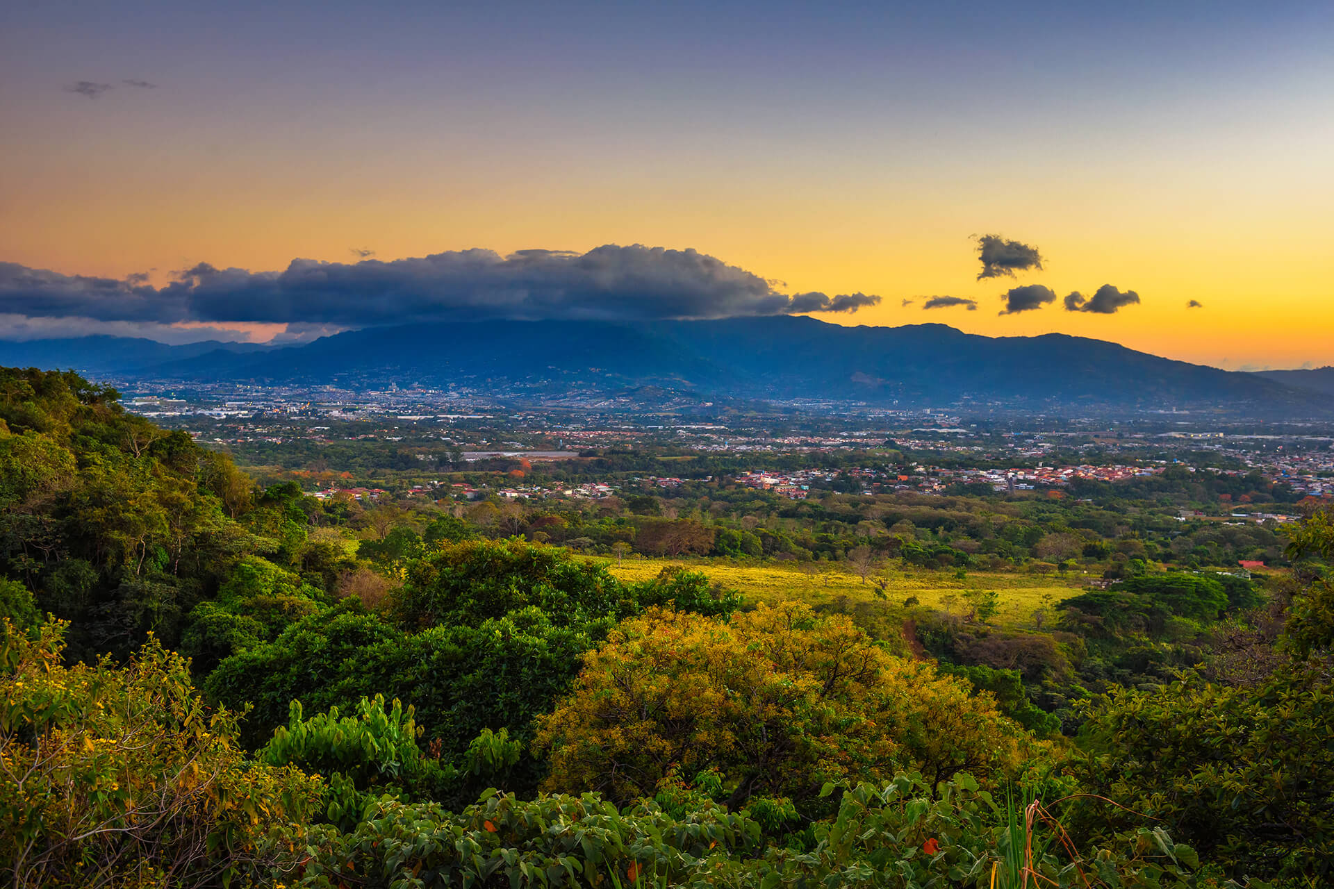 City of San José, Costa Rica’s capital, surrounded by mountains and a lush tropical forest, at sunset.