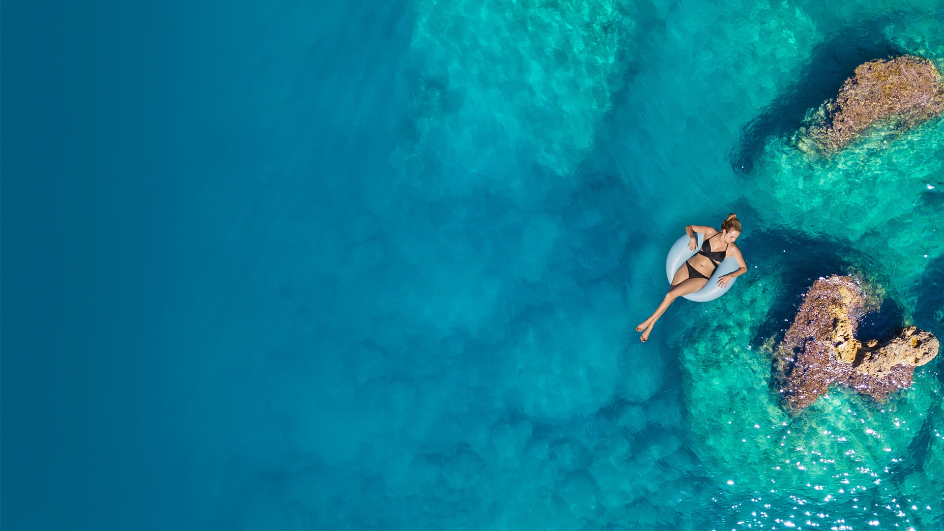 A woman in an inflatable tube is floating on a turquoise sea.